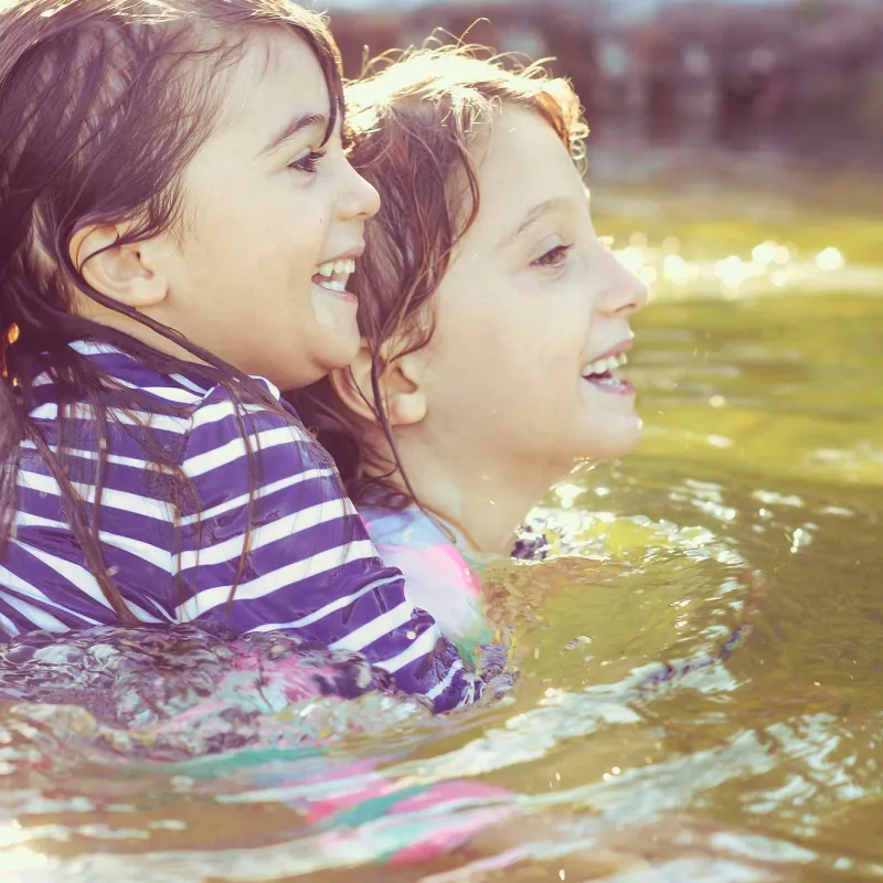 Two young children, one holding the other, swimming in a lake.