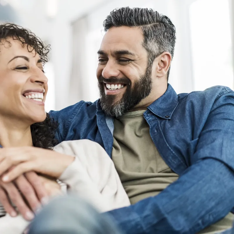 A couple laughing together on their couch at home. 