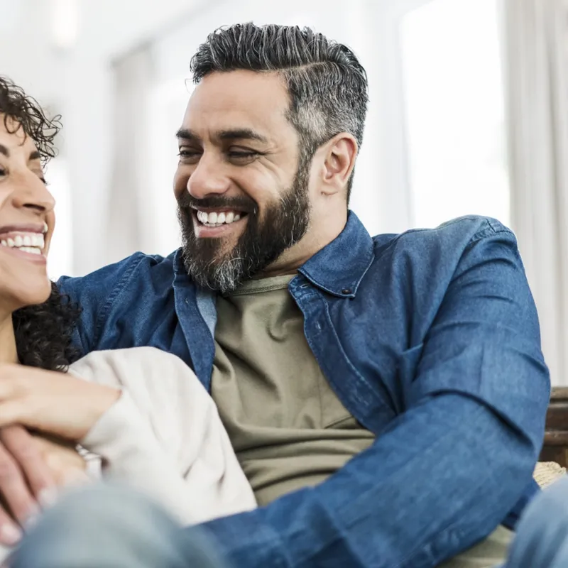 A couple laughs together on the couch.