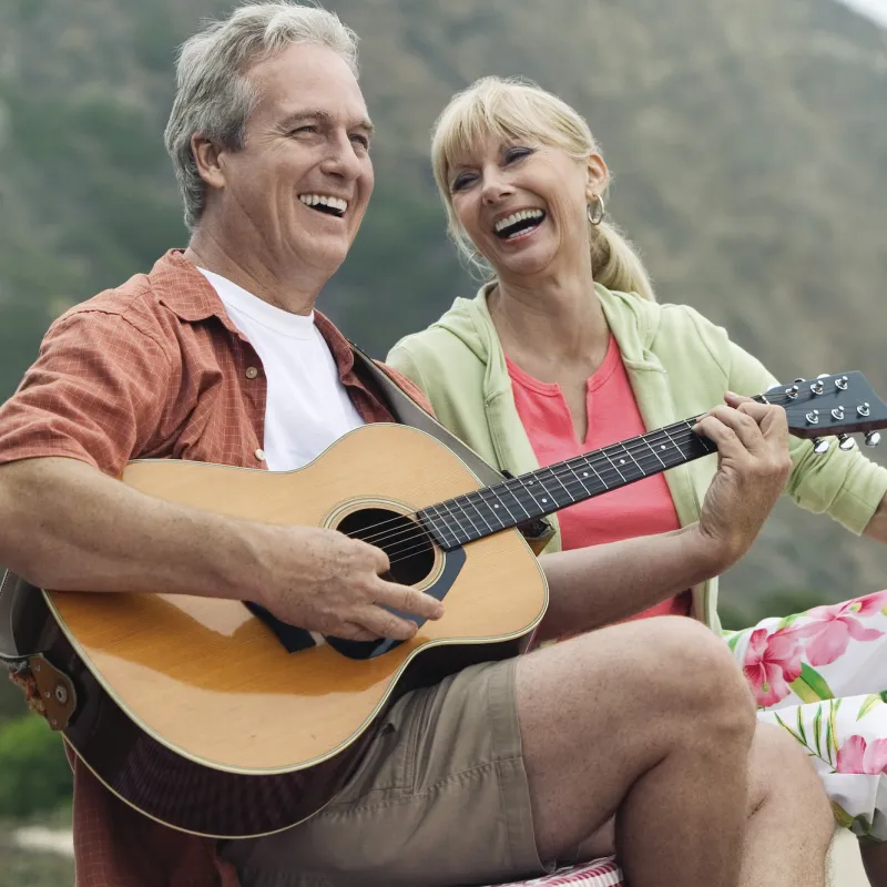 A couple playing guitar on the beach.