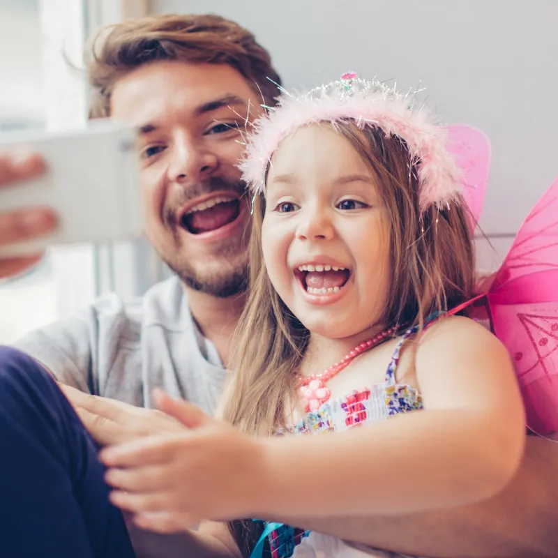 A dad and daughter take a selfie while playing dress up.