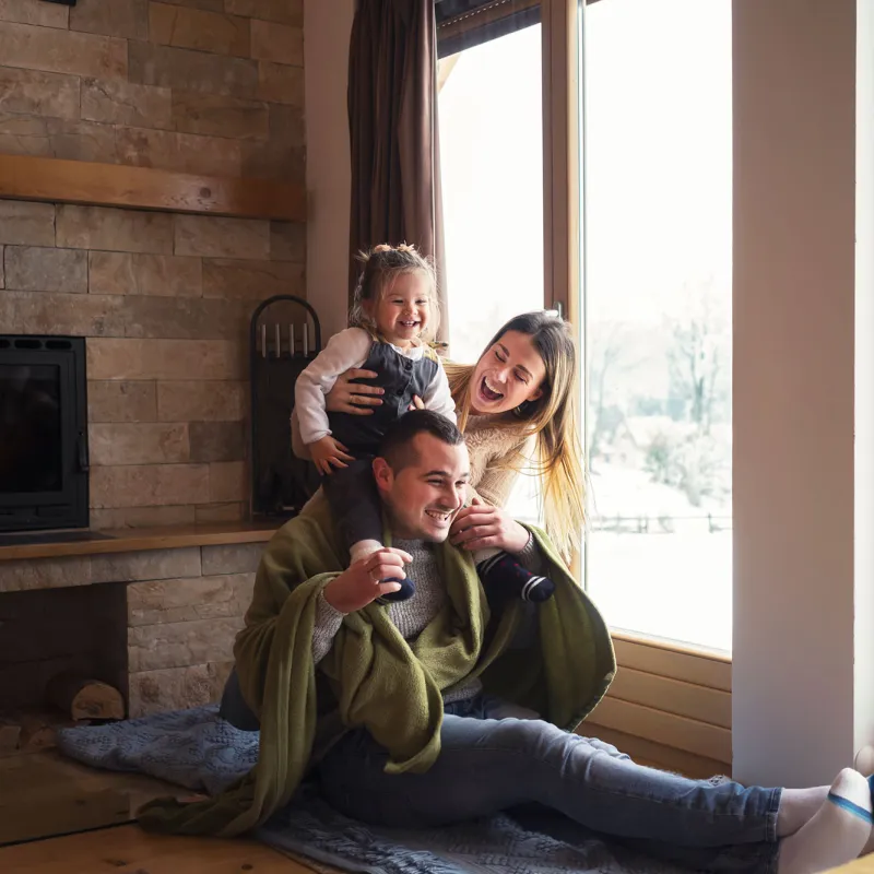 A young family plays together indoors by a window at home