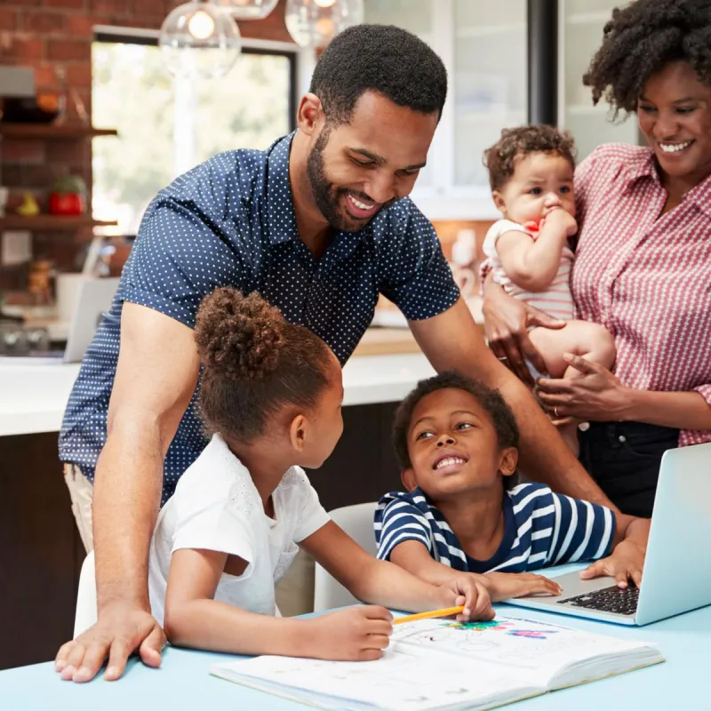 Photo of a family standing at a laptop making plans and smiling.