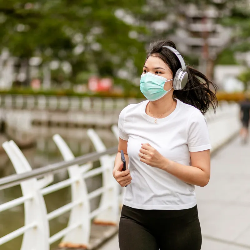 Woman running in a park outside while wearing a mask.