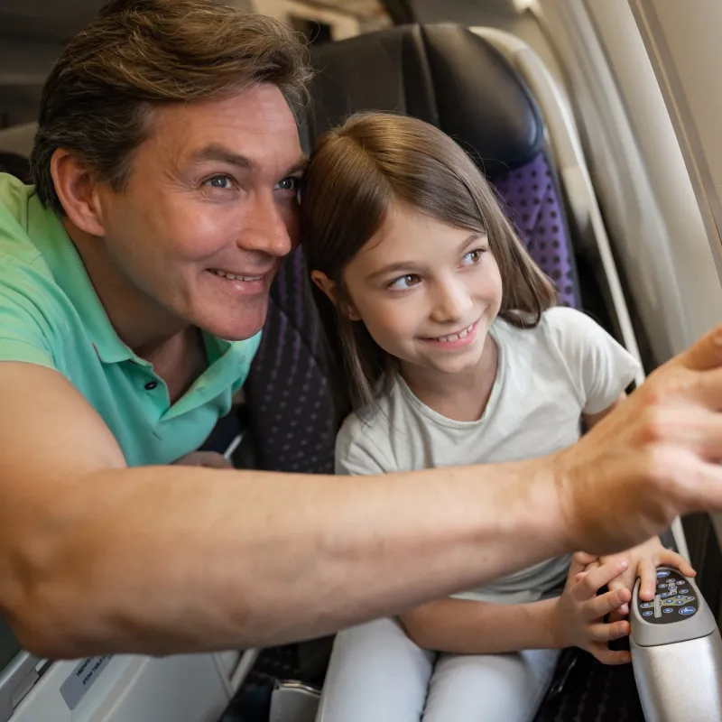 A father and daughter looking out the window of an airplane.