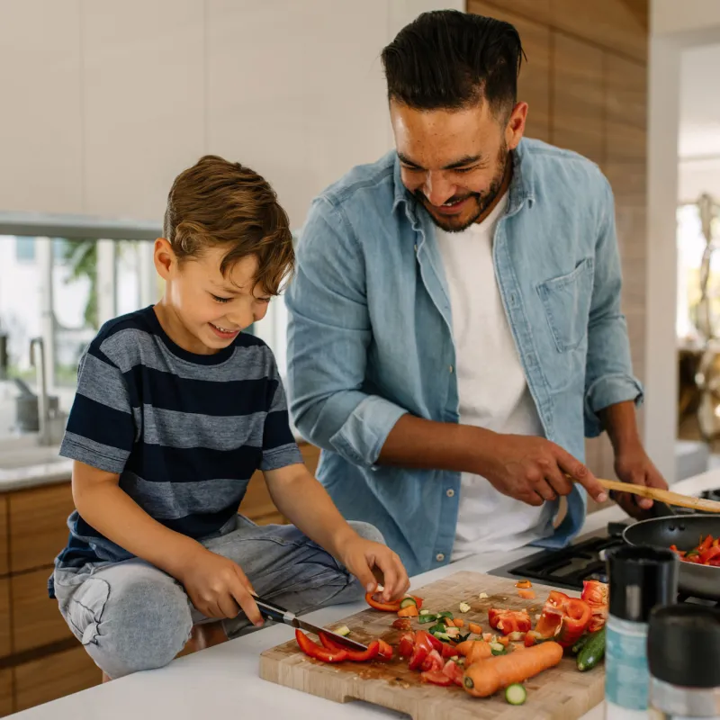 A father an son laugh together while preparing a healthy meal.