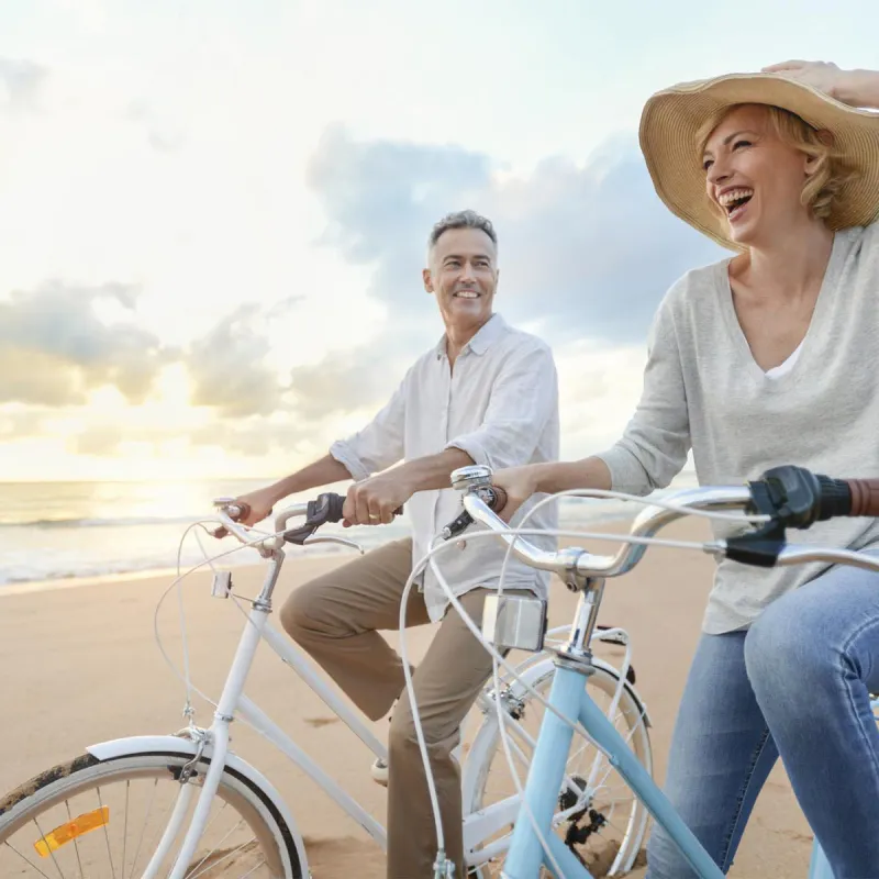 Man and woman in a hat riding bicycles on the beach at sunset. 