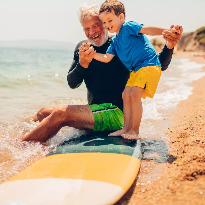 A grandfather teaches his grandson to surf.