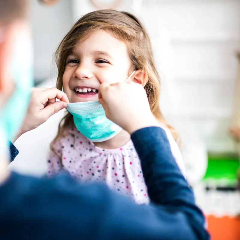 A happy little girl wearing a face mask.