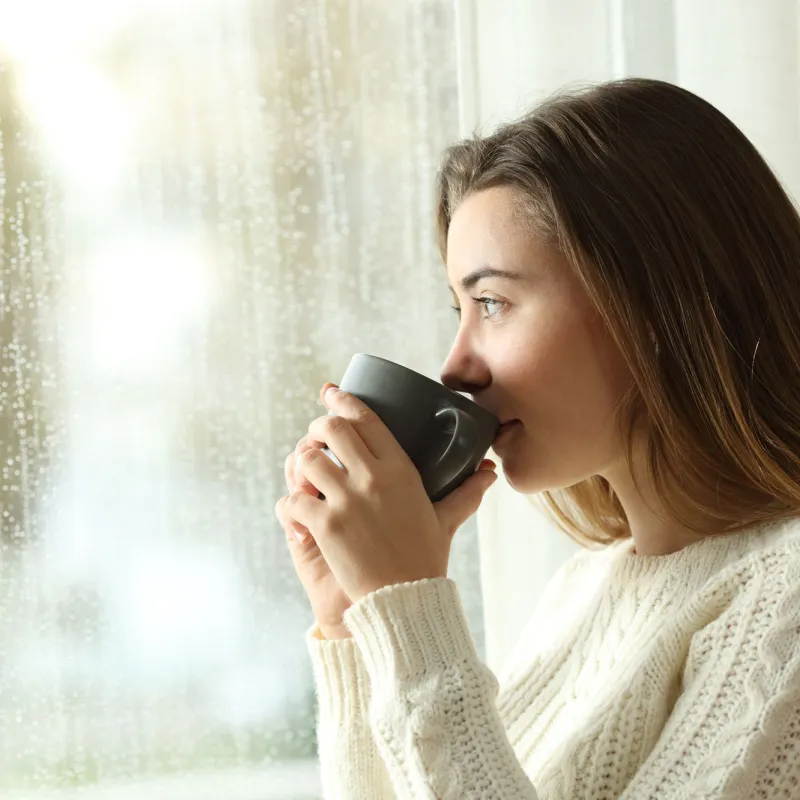 A woman drinking indoors while looking through the window