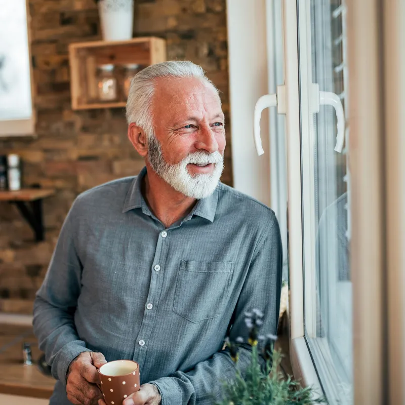 A man enjoying a cup of tea looking out the window.