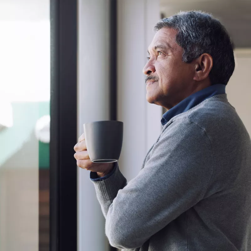 A man drinking coffee while looking outside from his window