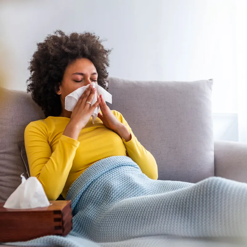 A woman sneezes on her couch at home