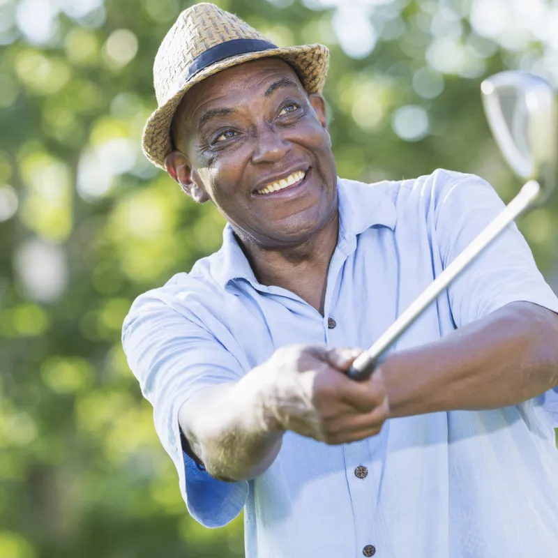 An older man swings a club on the golf course.