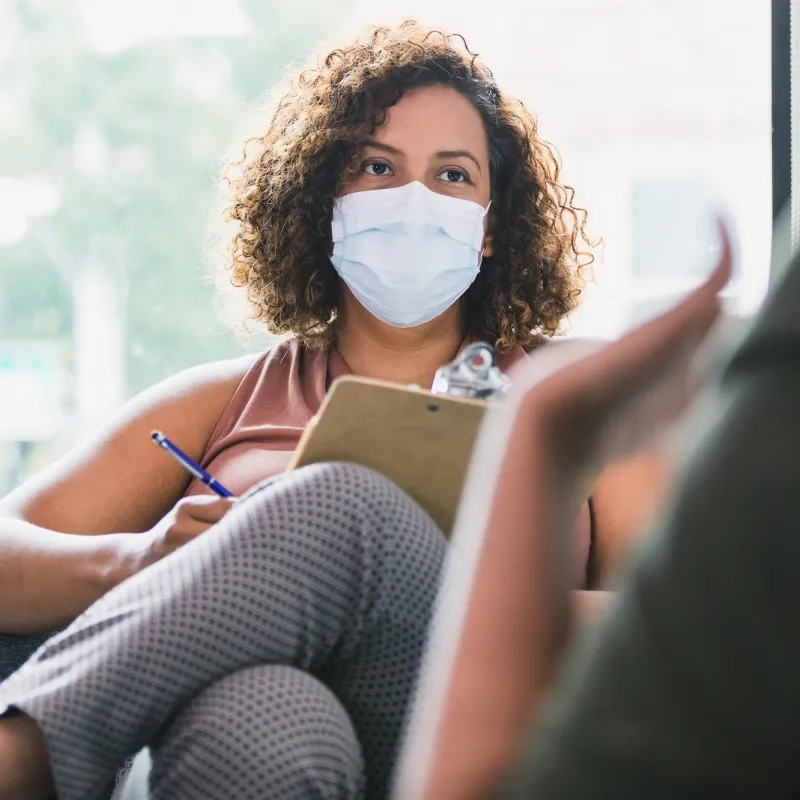 A mental health provider visits with a patient wearing a mask. 