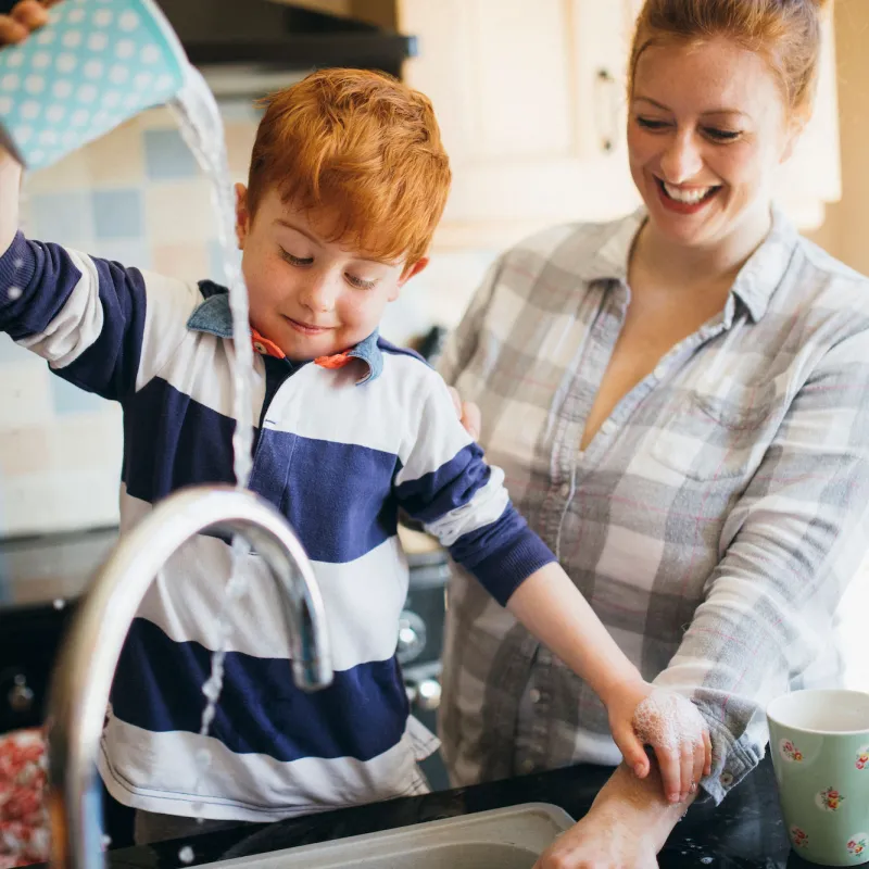 A mom and son wash dishes together.