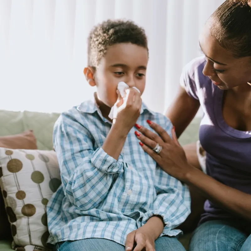 A mom comforts her son while he's sneezing at home.