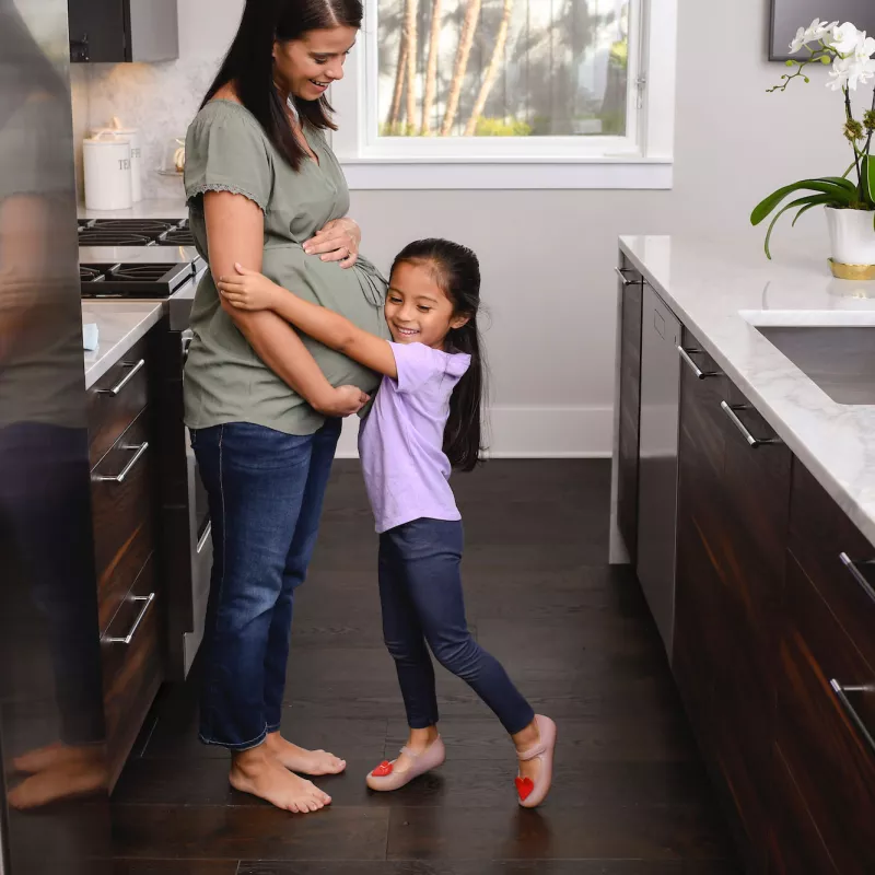 A pregnant mom and her daughter in the kitchen.