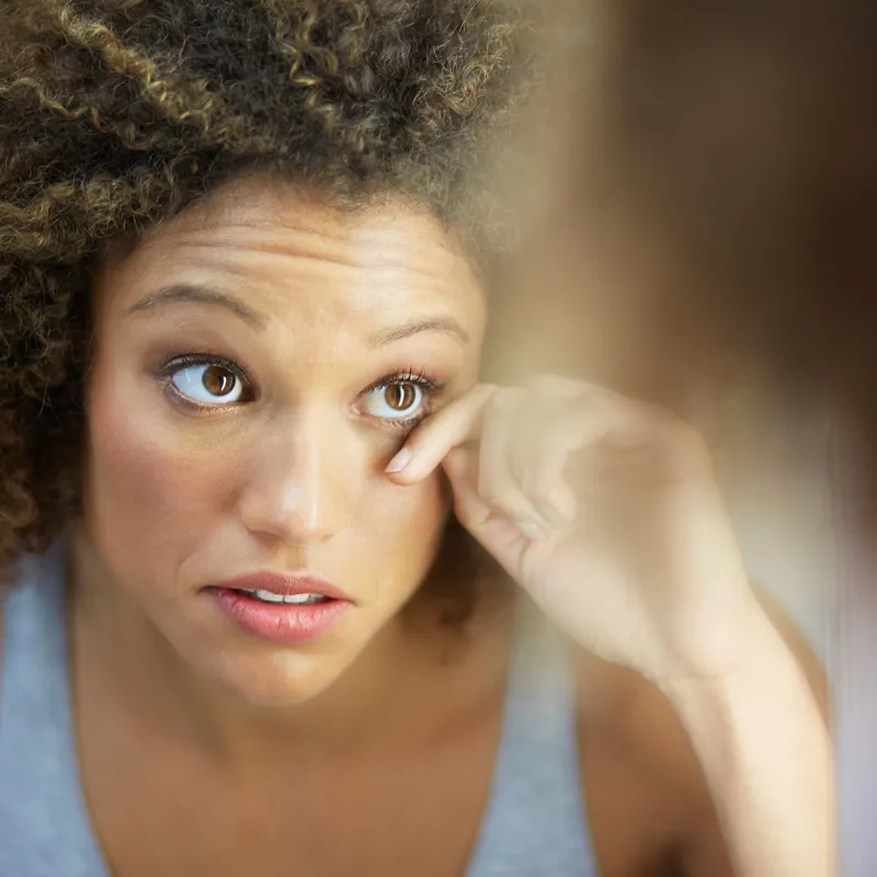 A woman examines her eye in a mirror.