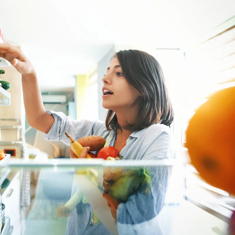 Young woman fills her arms with healthy vegetables at home