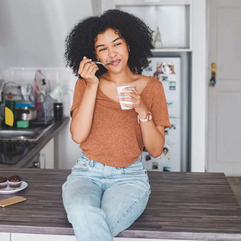 A woman sitting on her counter eating yogurt. 