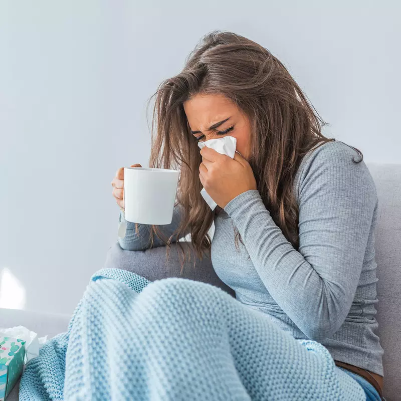 An adult woman sneezes into a tissue at home