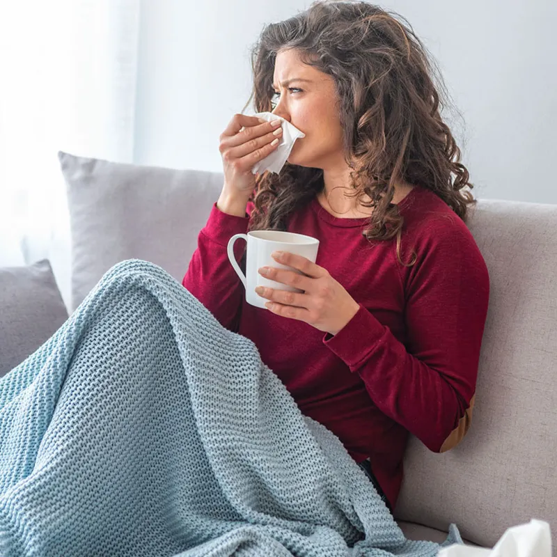 A woman on her couch blowing her nose. 