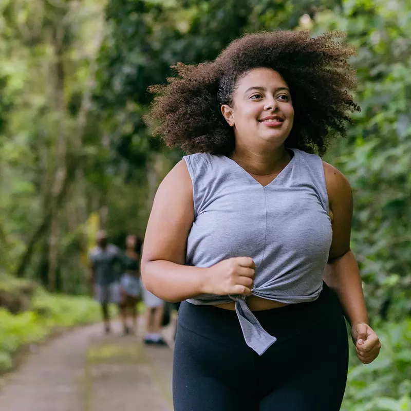 Hispanic woman running outdoors in a forest.