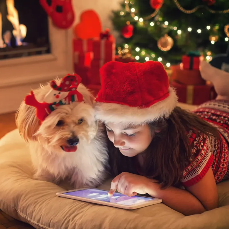 Young girl playing on tablet with dog next to her during the holidays