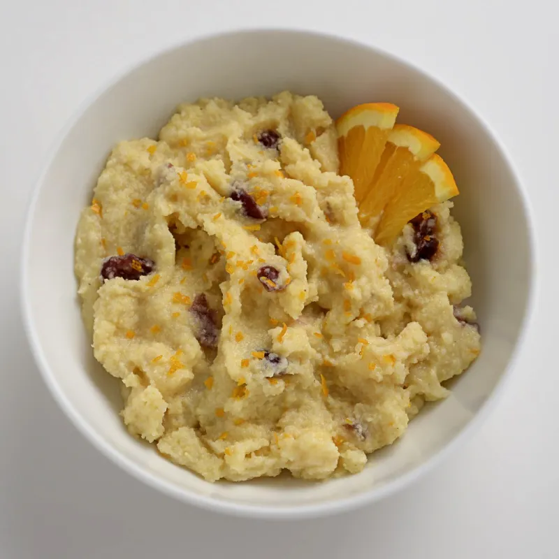 a bowl of polenta with dried cranberries and orange slices