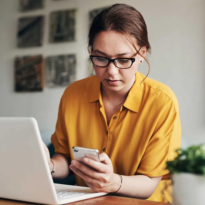 A woman on her laptop while using her phone