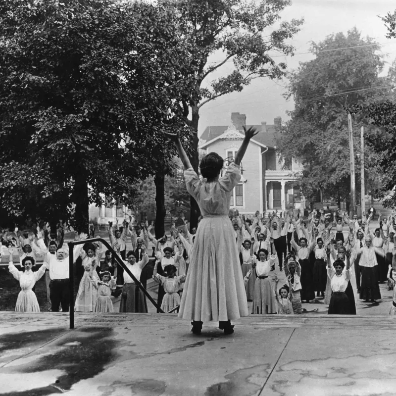 A woman leading out a group of people in breathing exercises while outdoors.