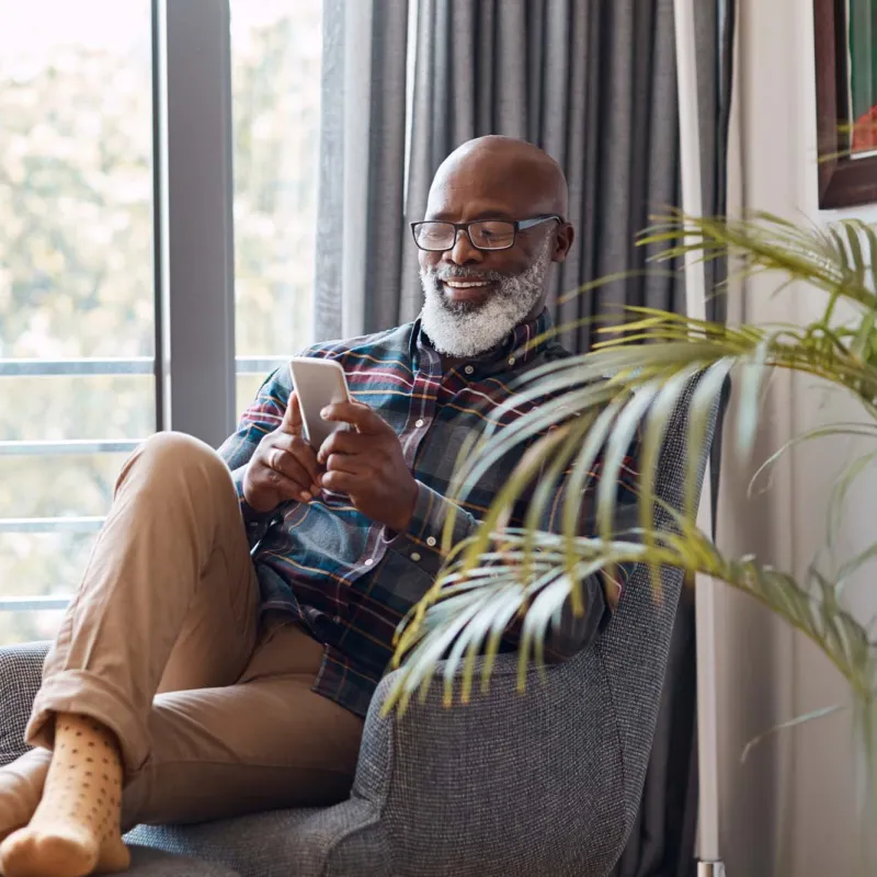 Older bearded man relaxing at home with phone