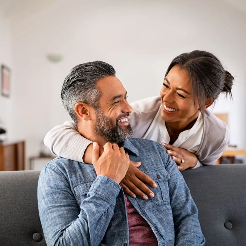 A man and woman laugh together in their living room. 