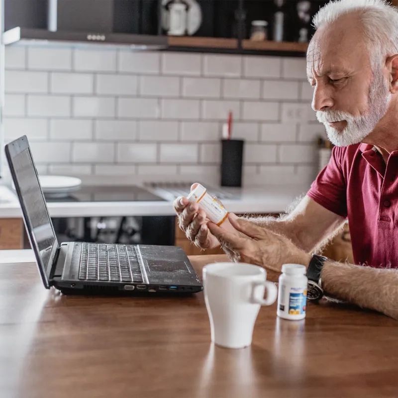 An older man requesting a prescription refill from his computer. 