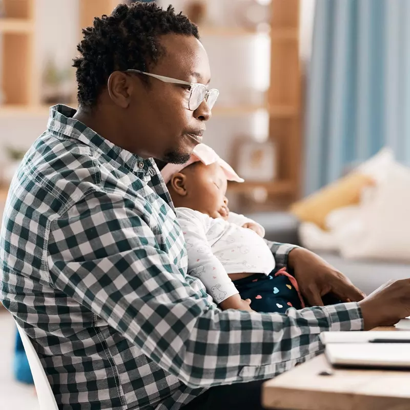 A father working on his computer with his infant on his lap.