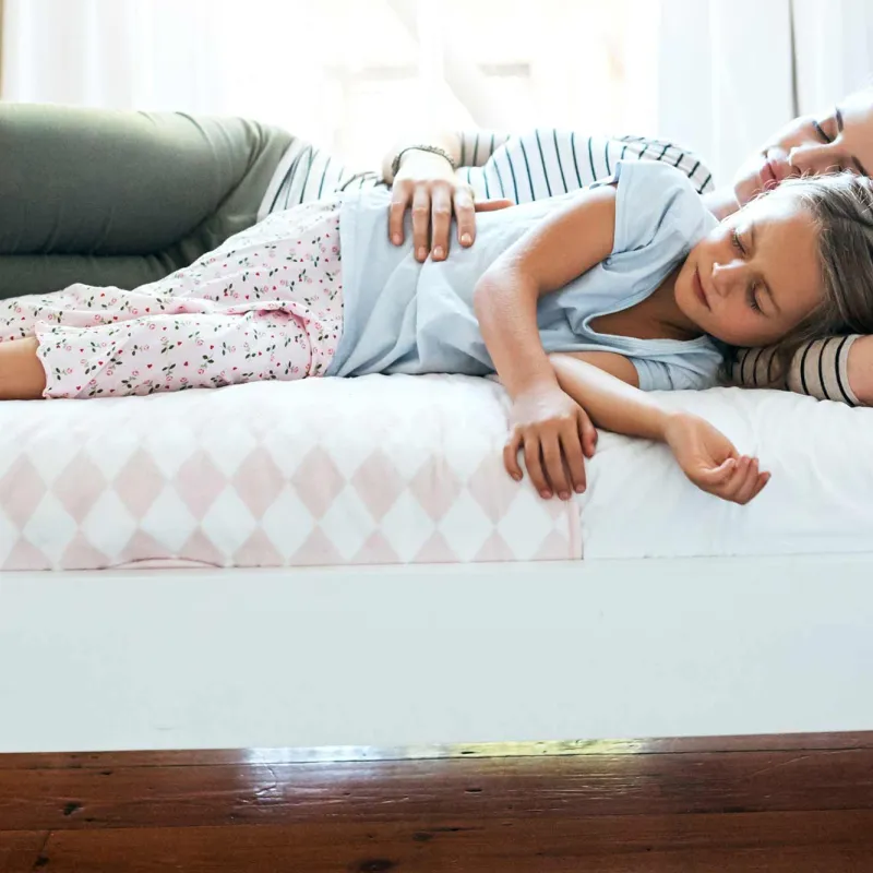 A mother and daughter laying down on a bed in their house