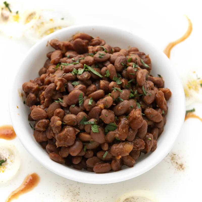 White bowl of baked beans on white, garnished counter