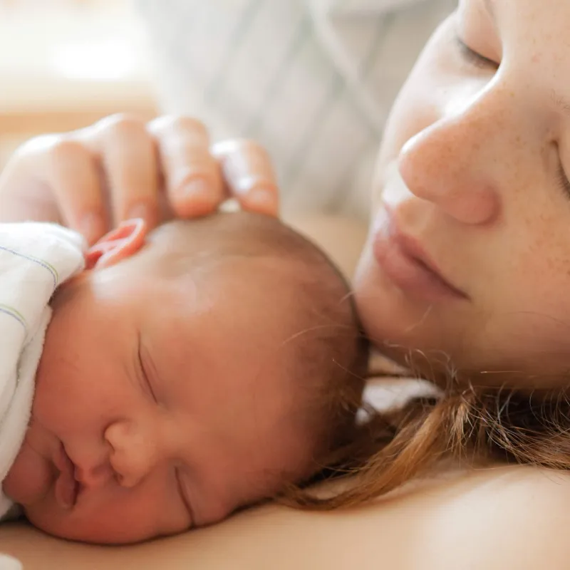 A serene mother cuddles with her sleeping newborn baby.