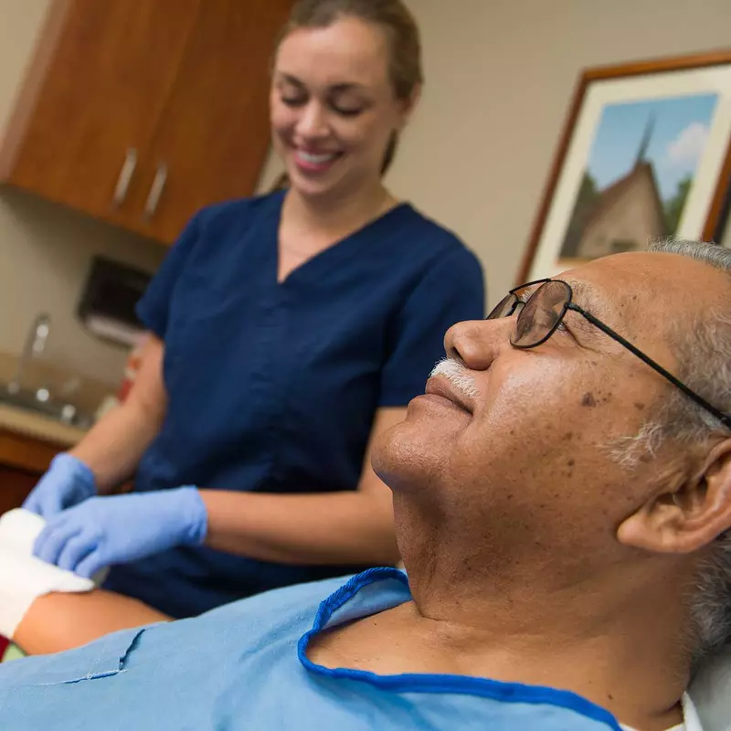 A nurse tends to a Hispanic man's wrist wound.