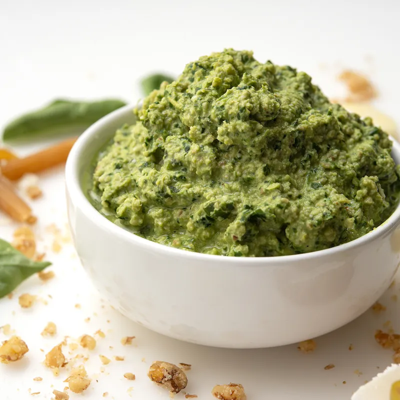 White bowl of green pesto on white counter