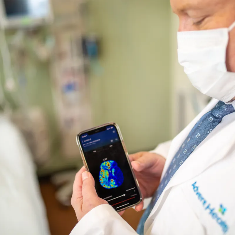 Physician holding a smartphone with a brain scan on screen.