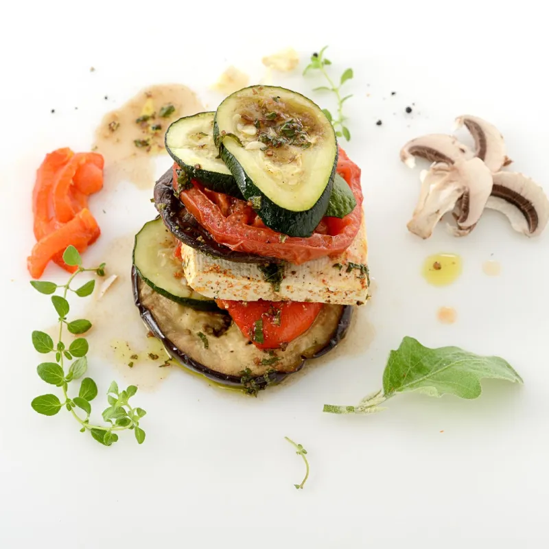 a stack of mushroom, tomato and eggplant and tofu slices, sprinkled with seasoning