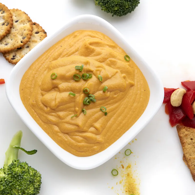 White bowl of orange cheese sauce next to crackers and broccoli.