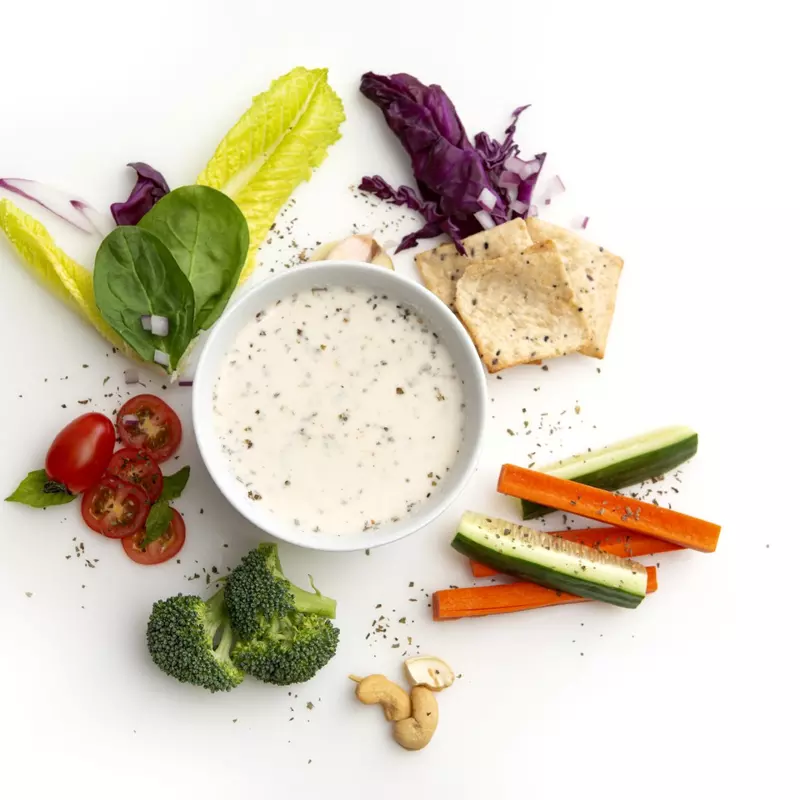 Cup of creamy ranch-style dressing surrounded by vegetables