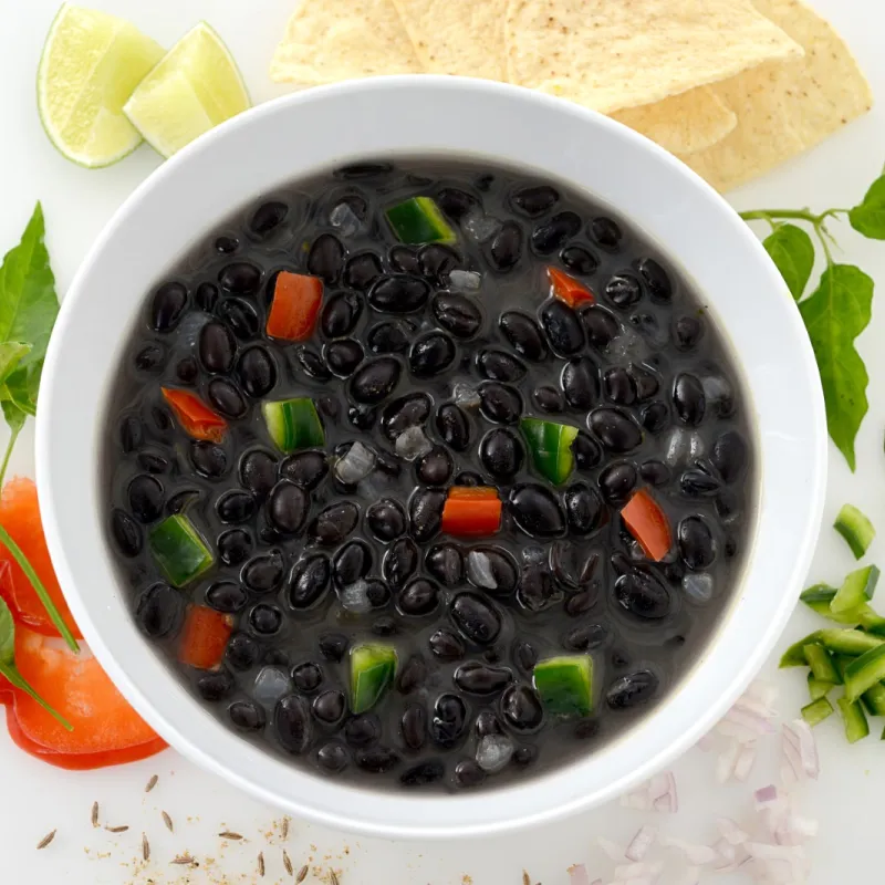 Bowl of cuban frijole stew surrounded by garnish, limes, and peppers