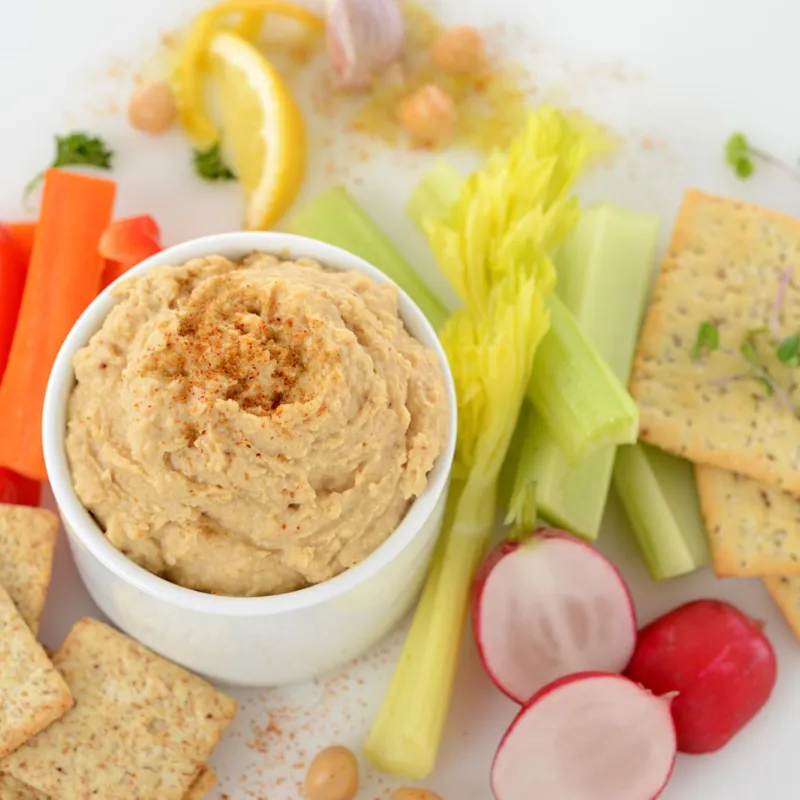 Dish of garmanzo hummus surrounded by crackers and vegetables