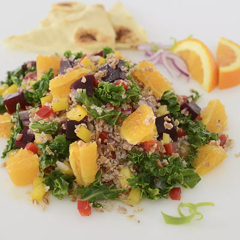 Mound of roasted beet, kale, and pepper salad with orange garnishes