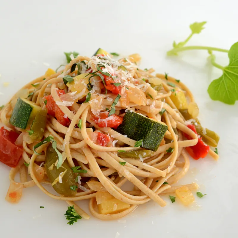 Mound of whole wheat pasta and veggies with leave garnish