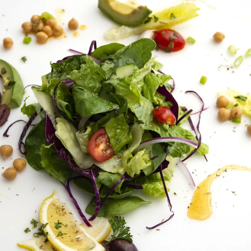 Mound of mixed green salad with tomato and lemon garnishes